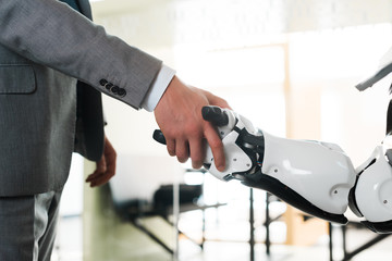 cropped view of businessman and robot shaking hands in office
