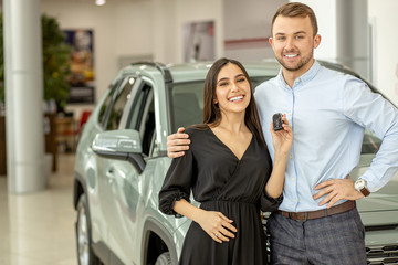 young caucasian beautiful couple buying their new first car in dealership, representative car in the background, happy owners of new jeep