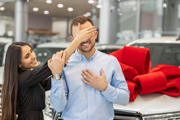 attractive caucasian brunette lady going to give new car as a gift to young man. woman stand...