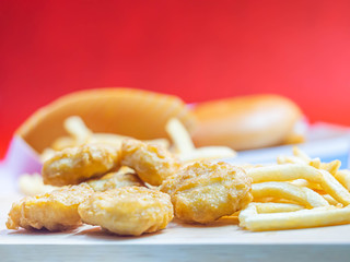 Closeup of crispy nuggets and french fried with blurry fish burger and red background.