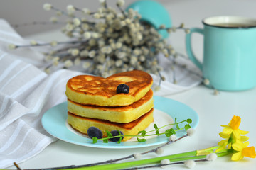 American pancakes on blue plate for healthy breakfast on white table with spring flowers.Breakfast on Valentine's Day or 8 March - pancakes in the shape of a heart.Pancake week.