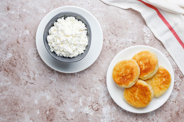 Cottage cheese pancakes.Russian syrniki or sirniki, cottage cheese fritters or pancakes with a bowl of fresh homemade cottage cheese on light background