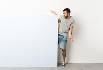 Young handsome man with beard holding a big blue empty placard unhappy for not understand something