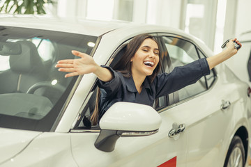 cheerful caucasian woman sit inside of new car, young woman smile, feel happy to have newly bought car. woman stuck out her hands and face