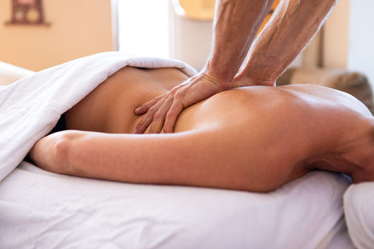 A young lady receiving Santosh massage in a cosy home environment. Spa body massage. Strong hands of professional male masseur doing gentle back massage