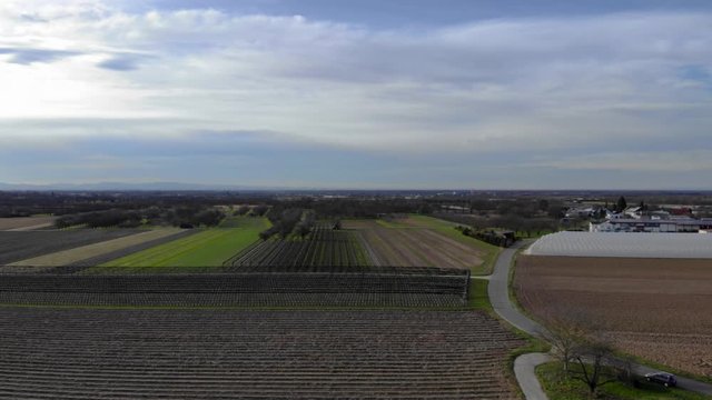 Aerial view of farmland and trees next to a village during daytime. Aerial dolly in.