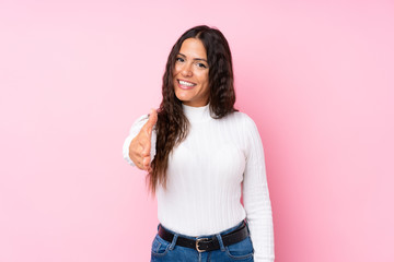 Young woman over isolated pink background shaking hands for closing a good deal