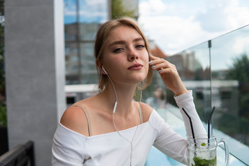 Porteait of blond woman blogger with cocktail is listening music or e-book on smartphone connected...