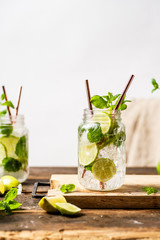 Refreshing mojito drink in glass jar with paper straws. Wooden table. White background 