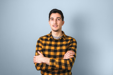 handsome looking guy in yellow square shirt with arms crossed on light-blue background