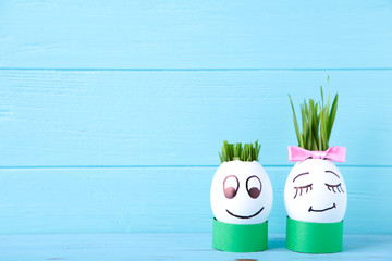 Cute handmade eggs with hair of green grass with copy space. Easter concept on blue background