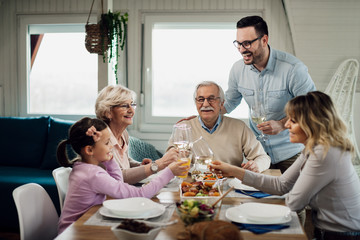 Cheerful multi-generation family toasting during a lunch at dining table.