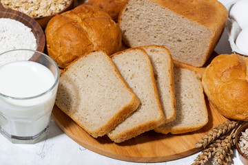 assortment of varied fresh bread, glass of milk on white background, closeup