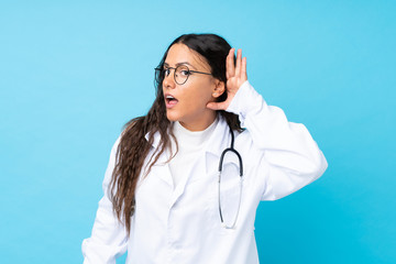 Young doctor woman over isolated blue background listening something