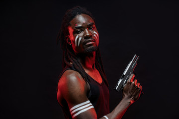 dreadful african gangster man with gun in hands, he has muscular body and dreadlocks on head. dangerous man inspires fear, ready to kill using cold steel arms. isolated black background