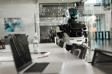 selective focus of humanoid robot standing near desk in conference hall
