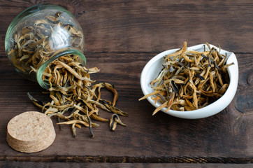 Golden buds. Chinese black tea from small bottle on wooden background.