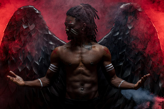 Dark African Angel With Big Black Wings Isolated, Young Serious Muscular Man Wearing Big Wings On The Back. Strong Angel Come Down From Heaven. Fantasy