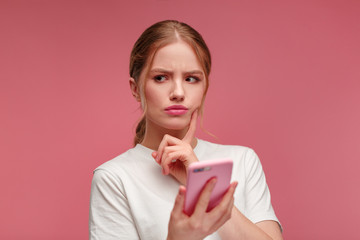 Confused young redhead woman holding pink smartphone.Embarassed girl has problem with broken not...