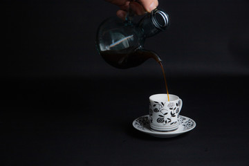 Hot black coffee and coffee jug falling on white porcelain cup
