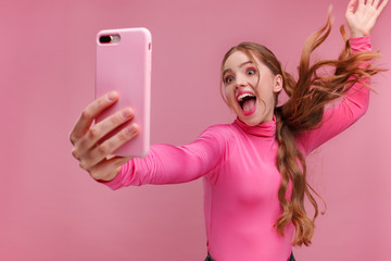 Funny young redhead woman making selfie. Smiling girl wearing pink blouse holding pink smartphone,...