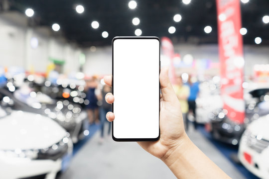 Mock up mobile phone. Hand holding mobile phone with abstract blurred cars exhibition show background image. Car shopping online, internet and social network background concept.