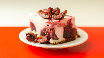 Japanese cheesecake with cherry sauce and fresh cherries on the ceramic plate and red background
