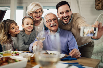 Cheerful multi-generation family taking selfie at dining table.