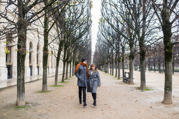 Young beautiful couple dressed stylishly, a girl in a gray coat, a man in a gray coat are walking in a park in Paris France