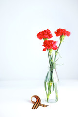 Three red carnations and St. George ribbon (Russian symbol) on a white uniform background. Greeting card for the holiday of the great victory of May 9.