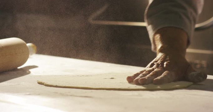White flour flying into air as pastry chef in black suit slams ball dough on white powder covered table