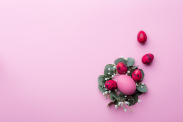 Bright burgundy quail eggs in eucalyptus twigs and gypsophila flowers on a pink paper background. Easter holiday concept. Copy space