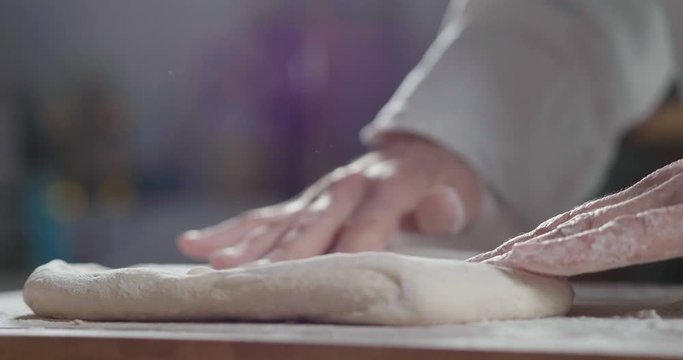 White flour flying into air as pastry chef in black suit slams ball dough on white powder covered table