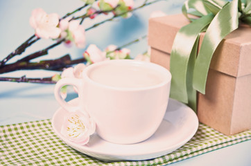 A cup of tea, gift box and cherry blooming with flowers sakura on the blue background. Spring concept.