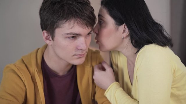 Close-up of brunette Caucasian woman whispering on ear of teenage boy. Mother sharing secrets with teen son. Trust, unity, reliance, lifestyle.