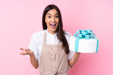 Young woman with a big cake over isolated background with shocked facial expression