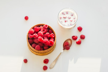 Raspberries in bowl with cup of milk on white background. Top view