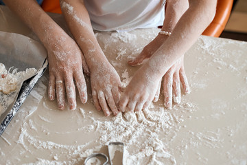 woman and girl's hands going to kneading the dough. close up cropped photo.household chores. lifestyle, free time, spare time
