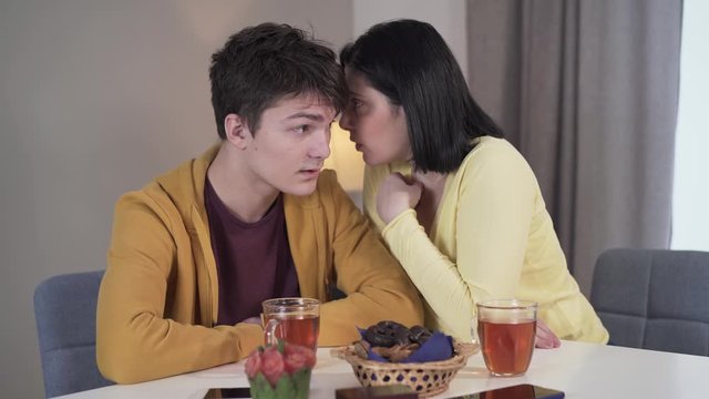 Portrait of adult Caucasian mother sharing secrets with teenage son. Wise brunette woman whispering on ear of teenage boy. Family, reliance, trust, lifestyle.