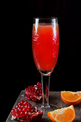 Red cocktail with champagne and fruit syrup in a champagne glass against the black background