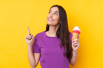 Young brunette woman with a cornet ice cream over isolated yellow background intending to realizes...