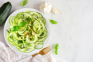 Healthy zucchini pasta topped with garlic and basil. Top view table scene on a white marble background.