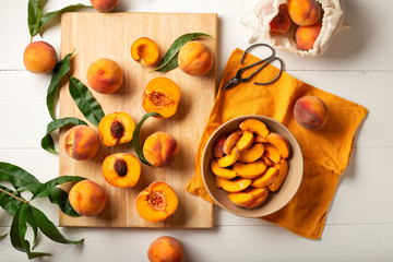 Peaches whole fruits with leaves, peaches in halves, peach slices on a white kitchen table. The process of making peach jam, cooking peach dessert on a cutting board. Pastry chef work place. Flat lay