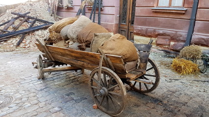 A sacked, rural horse-drawn cart loaded with bags stands on the street of a small vegetable garden....