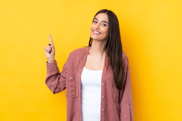Young brunette woman over isolated yellow background showing and lifting a finger in sign of the best