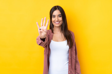 Young brunette woman over isolated yellow background happy and counting four with fingers