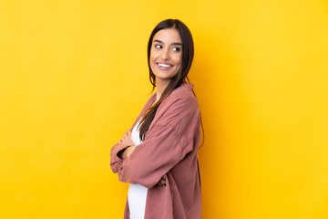 Young brunette woman over isolated yellow background with arms crossed and happy