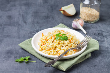 Vegetarian stewed side dish of brown rice in a white plate on a green linen napkin. Traditional national cuisine. Keto diet