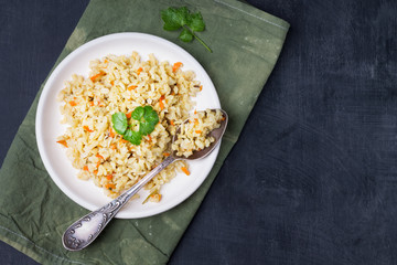 Vegetarian stewed side dish of brown rice with onions and carrots in a bowl on a light wooden background. Traditional national cuisine. Flat lay