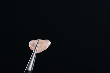 Macro shot of Himalayan salt crystal. Metal tweezers, black background, high resolution, hard light